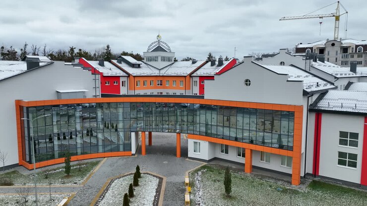 Front entrance to the building of unusual shape with mirrored windows. Beautiful new structure with courtyard. Grey sky at the backdrop.