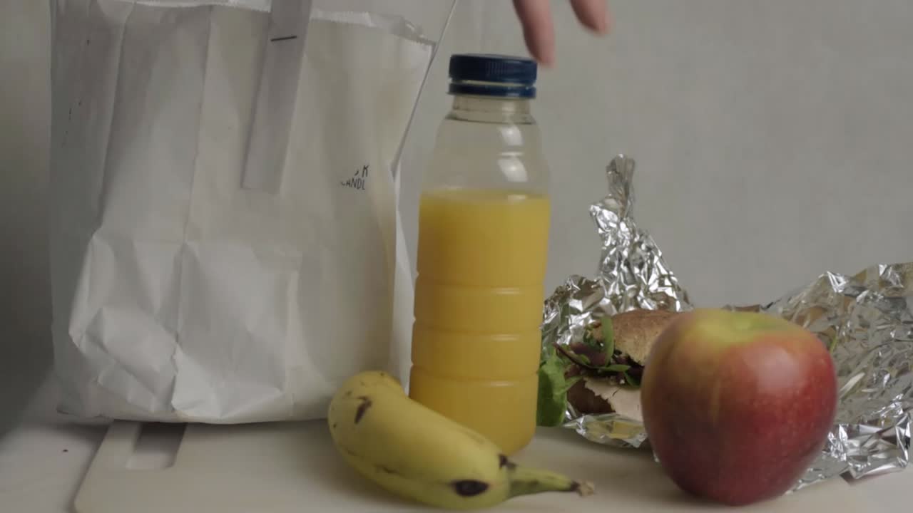 Packing a healthy lunch with sandwich and orange juice into a bag medium shot