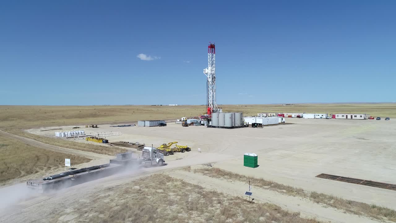 big rig recibiendo una entrega de tubería de un remolque de tractor en un camino polvoriento