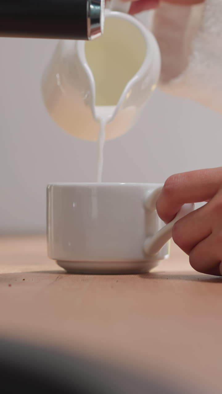 부에서 커피에 우유를 첨가하는 여자, 부드러운 망토를 입은 여자가 주말의 시작을 즐기고 있는 커피 컵에 우유 같은 거품을 첨가합니다.