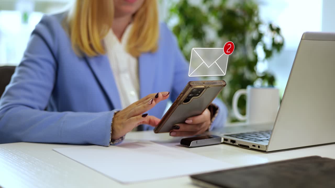 Woman reading emails and messages on a smartphone, sitting at her office desk