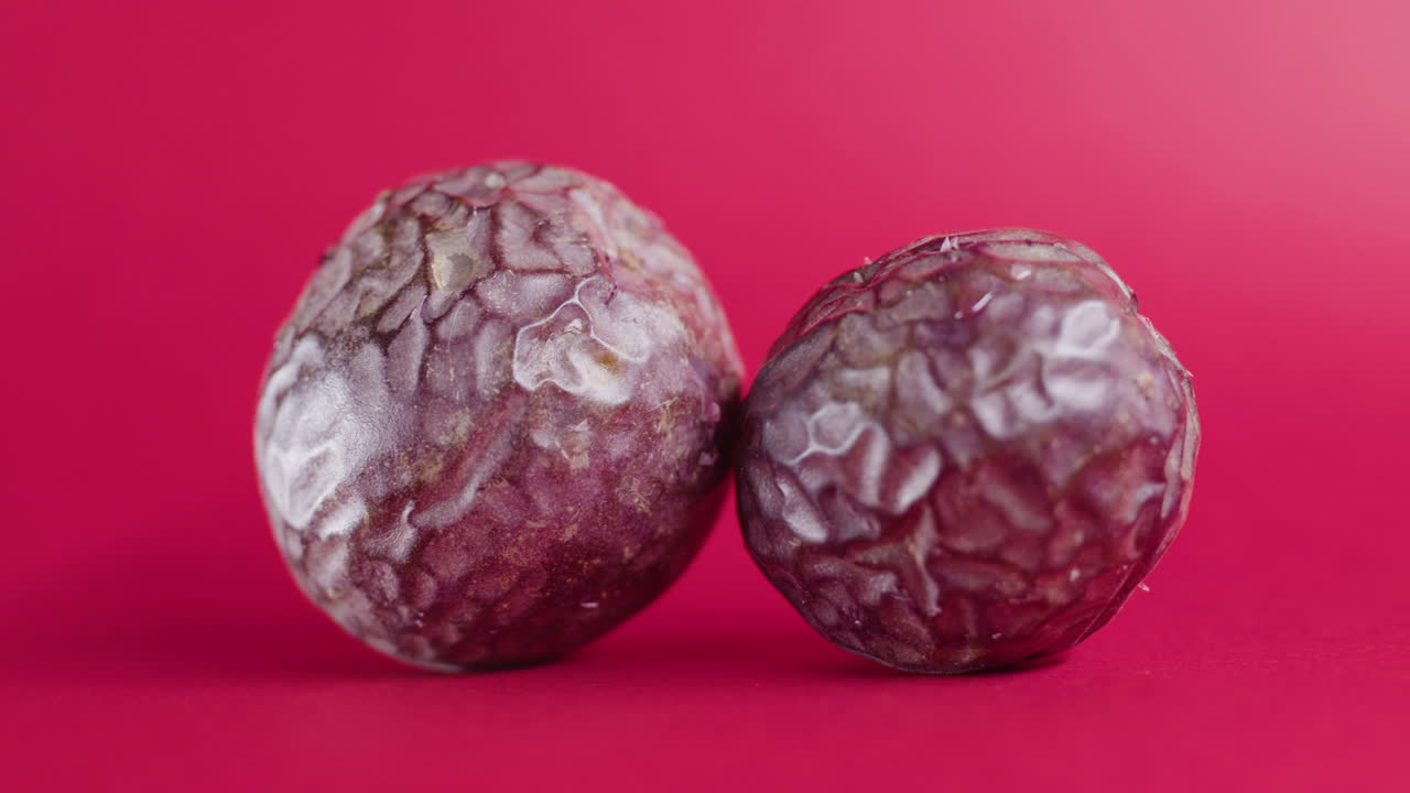 dos frutos de aguacate enteros rotando en una superficie rosa aislada
