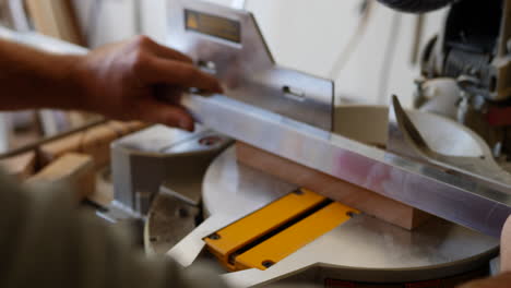 close up shot of the hands of a construction worker measuring and cutting a piece of angle iron on a metal chop saw in a workshop