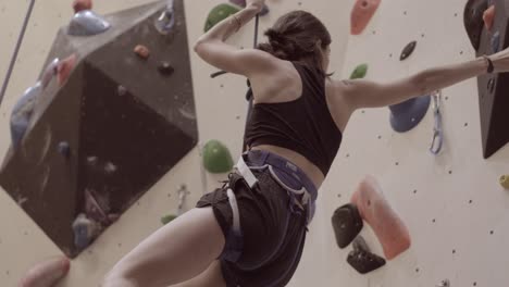 woman climbing and reaching the top of a outdoor bouldering wall with a rope