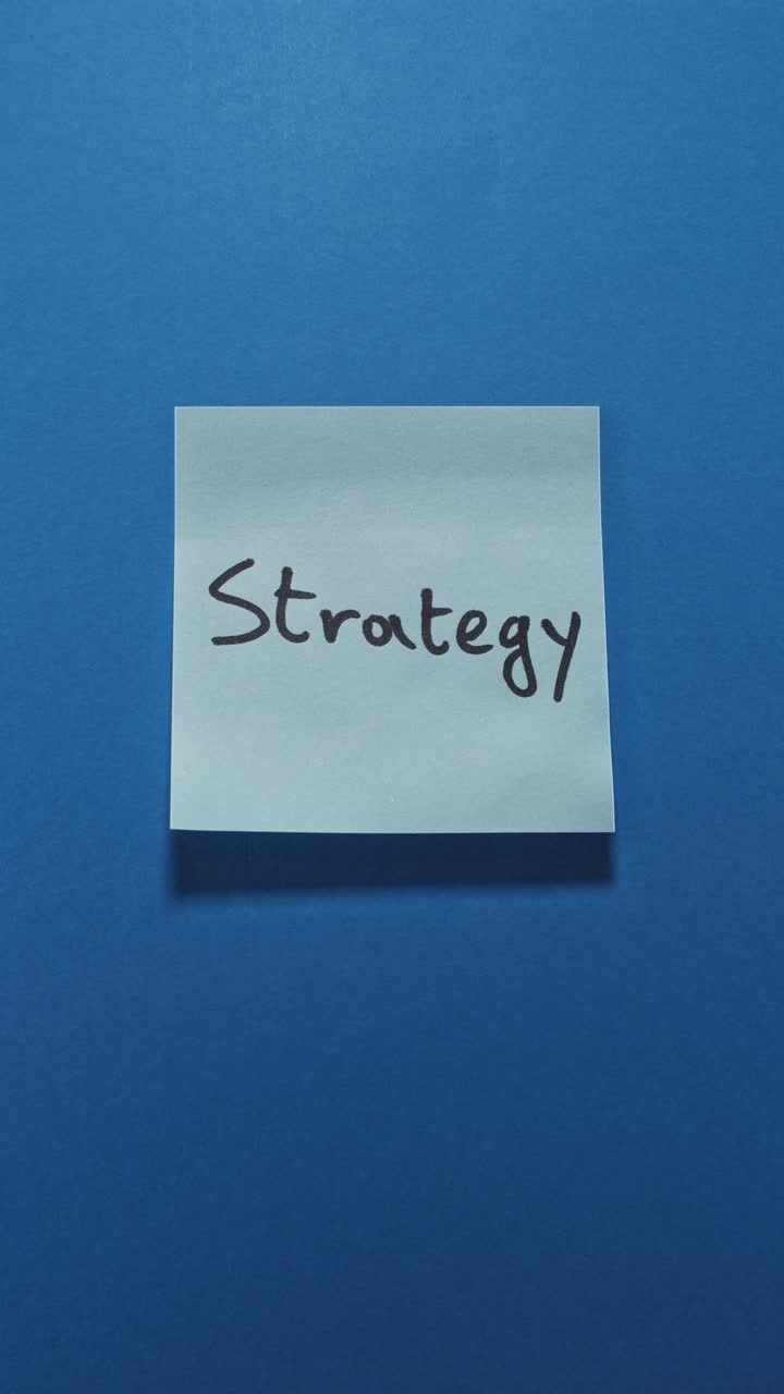 Hands posting Strategy sticky note on blue wall, illustrating planning