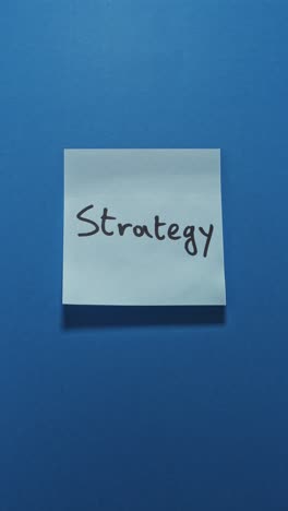 hands posting strategy sticky note on blue wall, illustrating planning