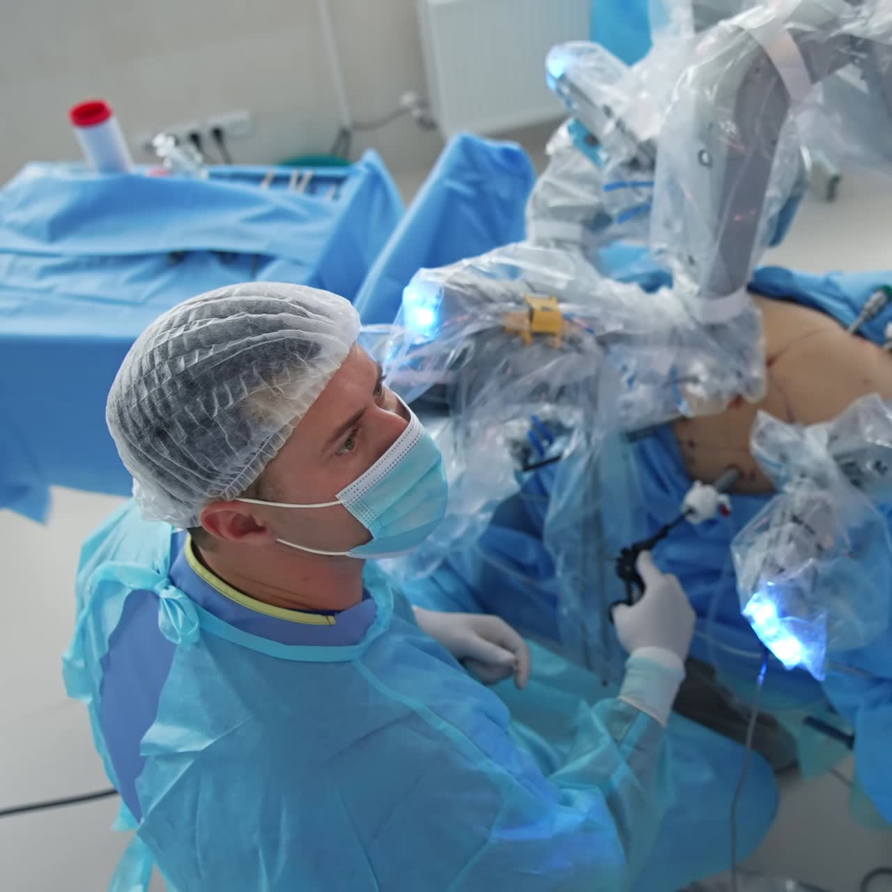 Minimally invasive surgery. Patient on a surgical table during operation involving robot in clinic. Doctor in medical uniform observes robotic surgery. Top view
