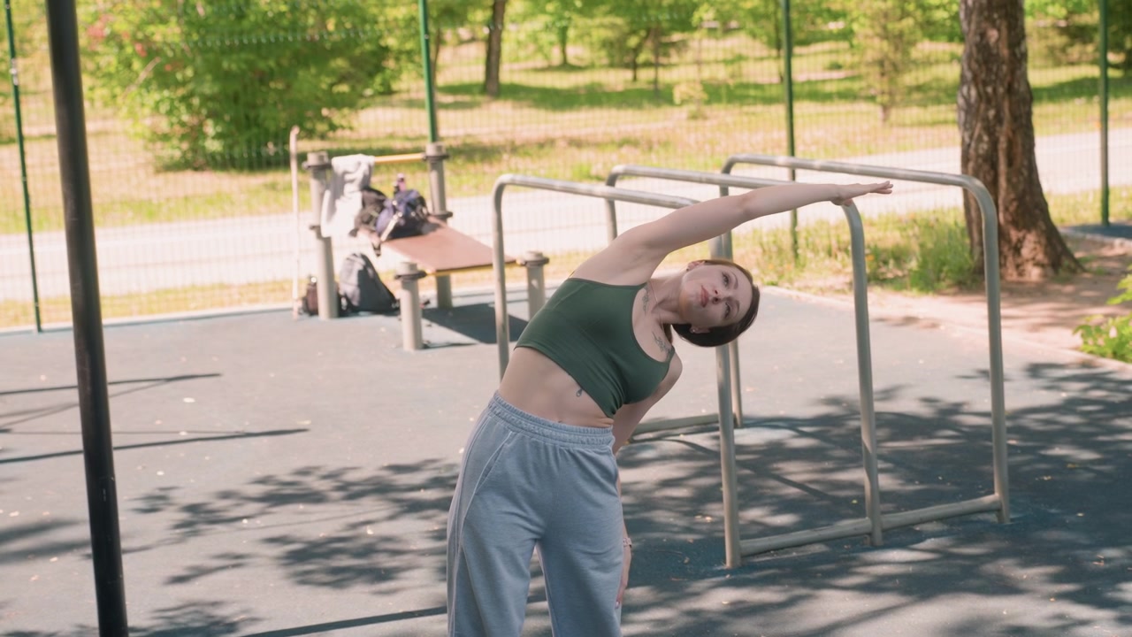 Close up of young woman performing various stretching exercises in outdoor park setting. Woman moves through different poses demonstrating flexibility and body control against backdrop