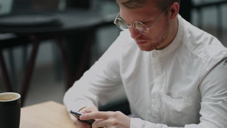 adult businessman texting on smartphone while sitting by laptop