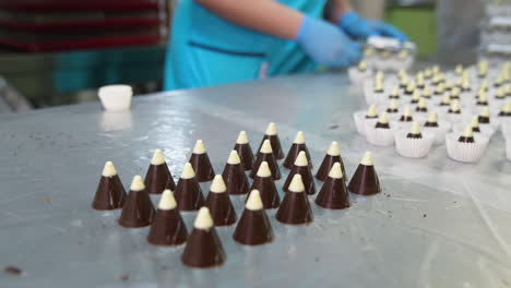 confectionery worker turns the plastic mold the table. cone chocolate candies with white tops are put on the metal surface. candies packaging at backdrop.