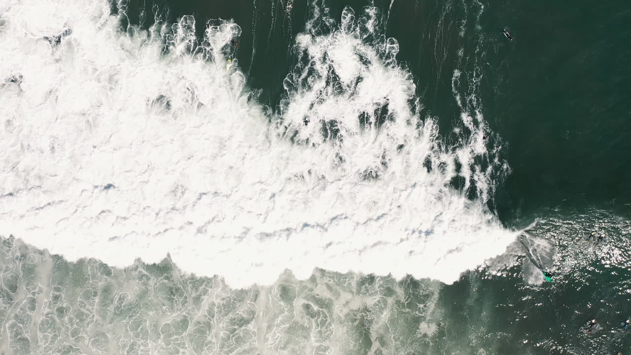Top-down aerial drone shot of people surfing and trying to catch waves in white water of the Spanish coast