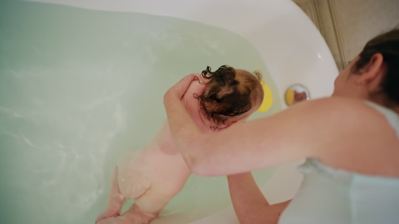 Top view of mother bathing baby in bathtub while playing with bath toys