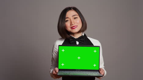 asian server presenting greenscreen display on laptop in studio