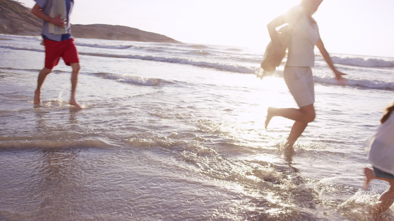 행복 한 가족 이 휴가 에 있는 해 가 지는 해변 에서 파도 에서 놀고 있다