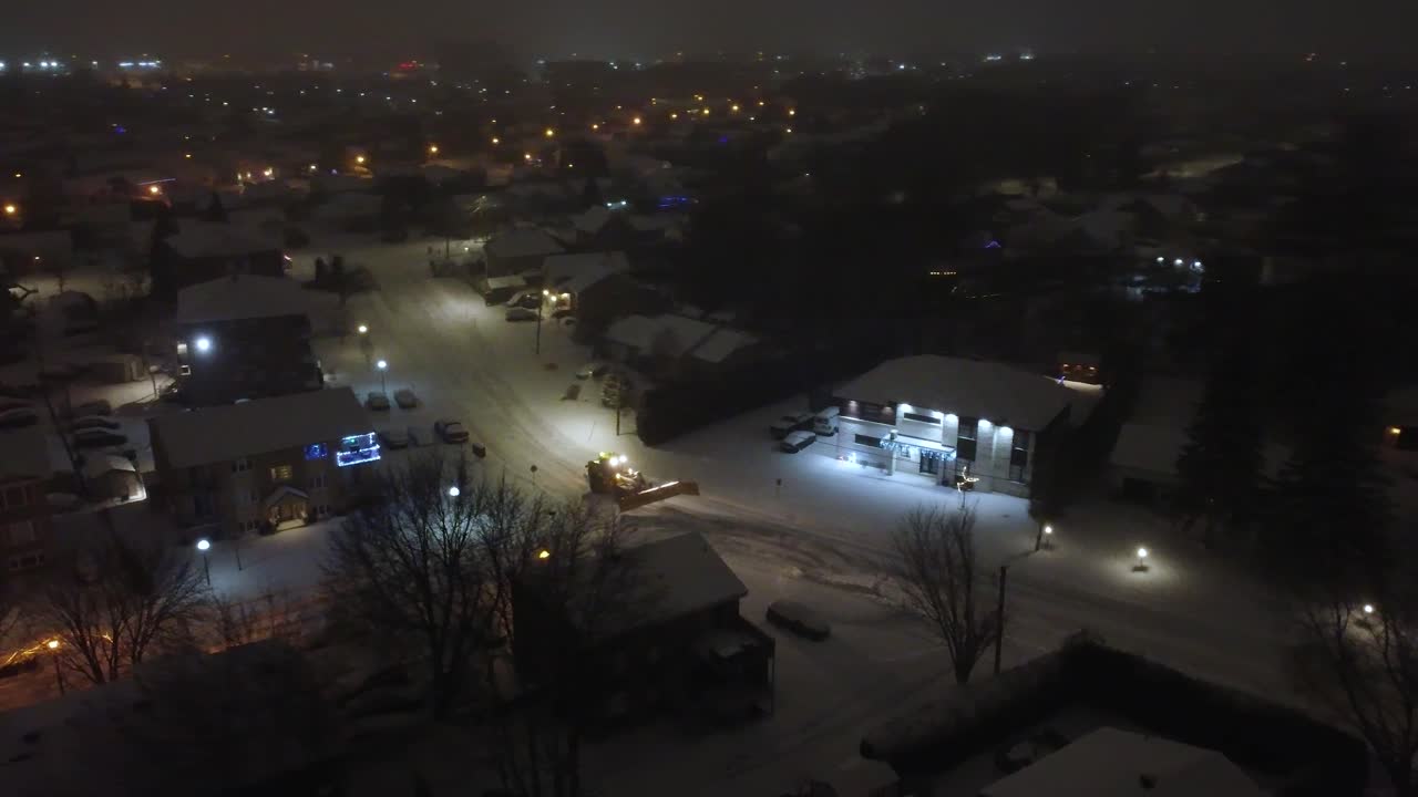 Snowplow Tractor Clearing Snow On Streets At Night In Canadian Neighborhood. Saint-Constant, Quebec, Canada. tracking drone shot