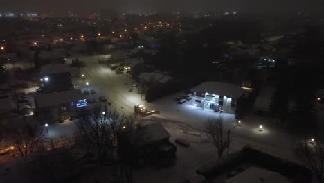 snowplow tractor clearing snow on streets at night in canadian neighborhood. saint-constant, quebec, canada. tracking drone shot