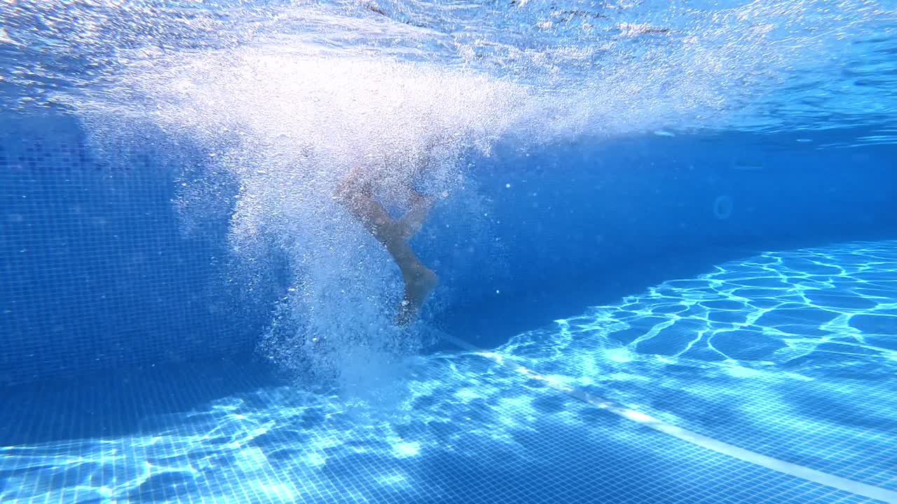 Underwater view with splash bubbles. Man jumps into the blue water in the swimming pool. Concept of sport, swimming pool, fitness.