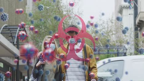 Animation-of-virus-cells-and-biohazard-sign-over-caucasian-couple-wearing-face-mask