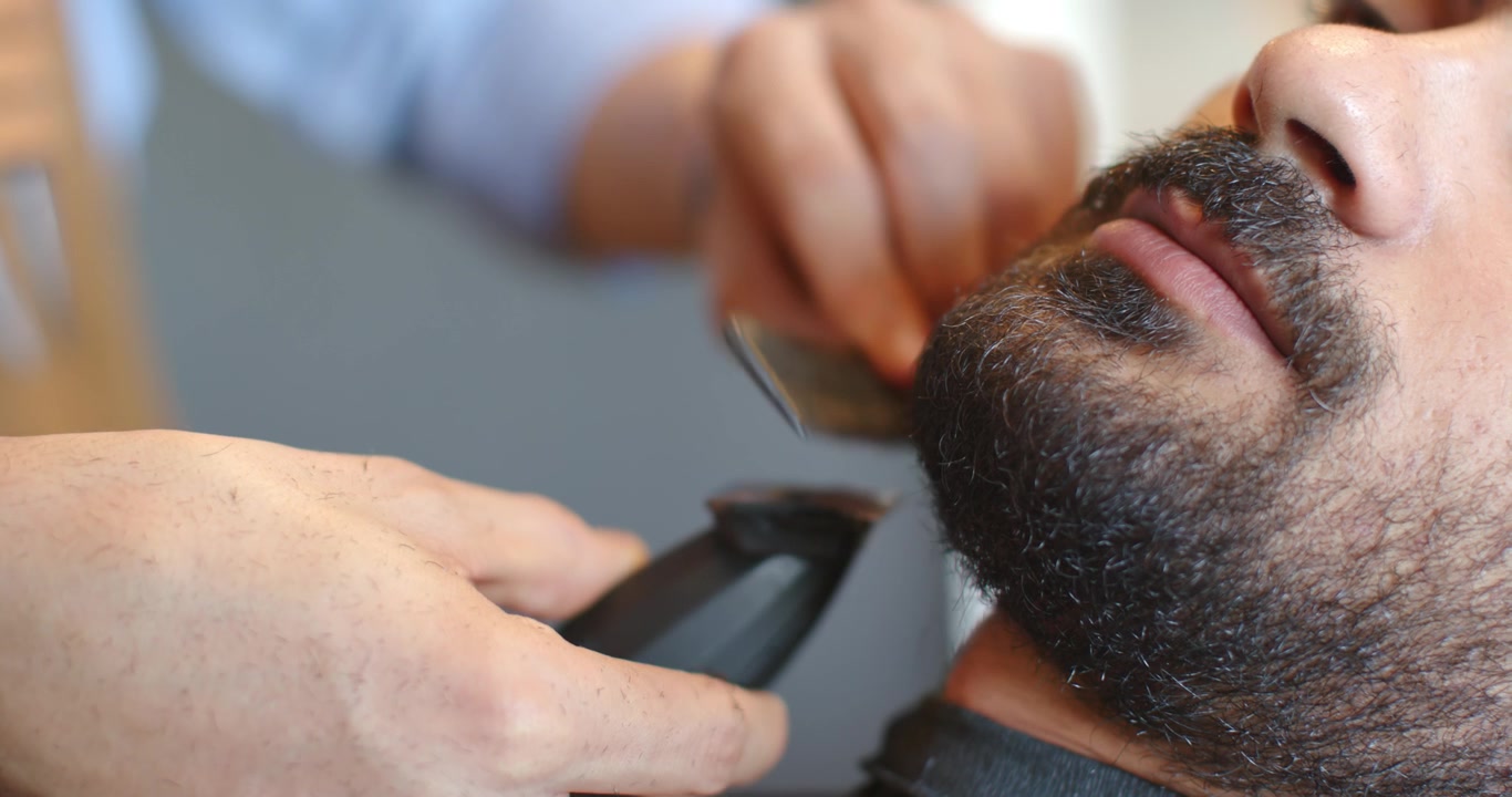 Barbeiro aparando a barba de cliente reclinado, modelando a borda com aparador, navalha na barbearia, com espaço para texto