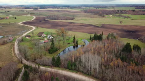 aerial shot of closing in to old rural family house, over some trees without leaves in autumn, road leading to it