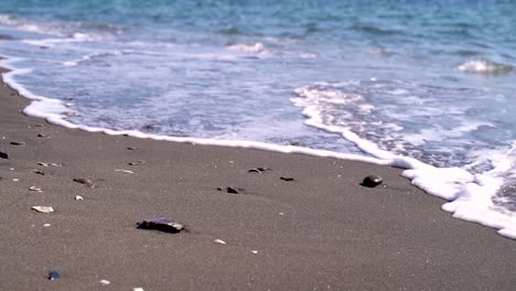 pequeñas olas moviendo guijarros en la playa de arena