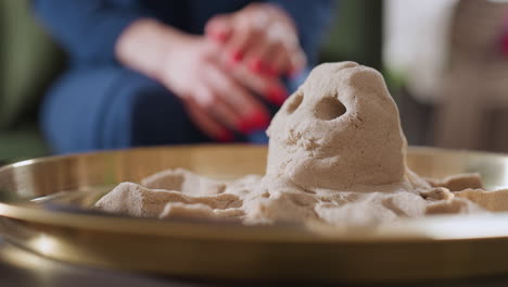 round angle captures detailed octopus figure molded in sand on tray, with blurred background featuring person seated in blue gown, highlighting tactile creativity and therapeutic ambiance