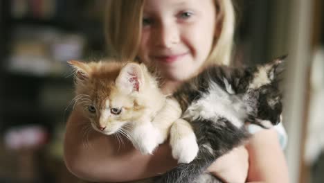 a little girl smiling and holding two kittens in her arms