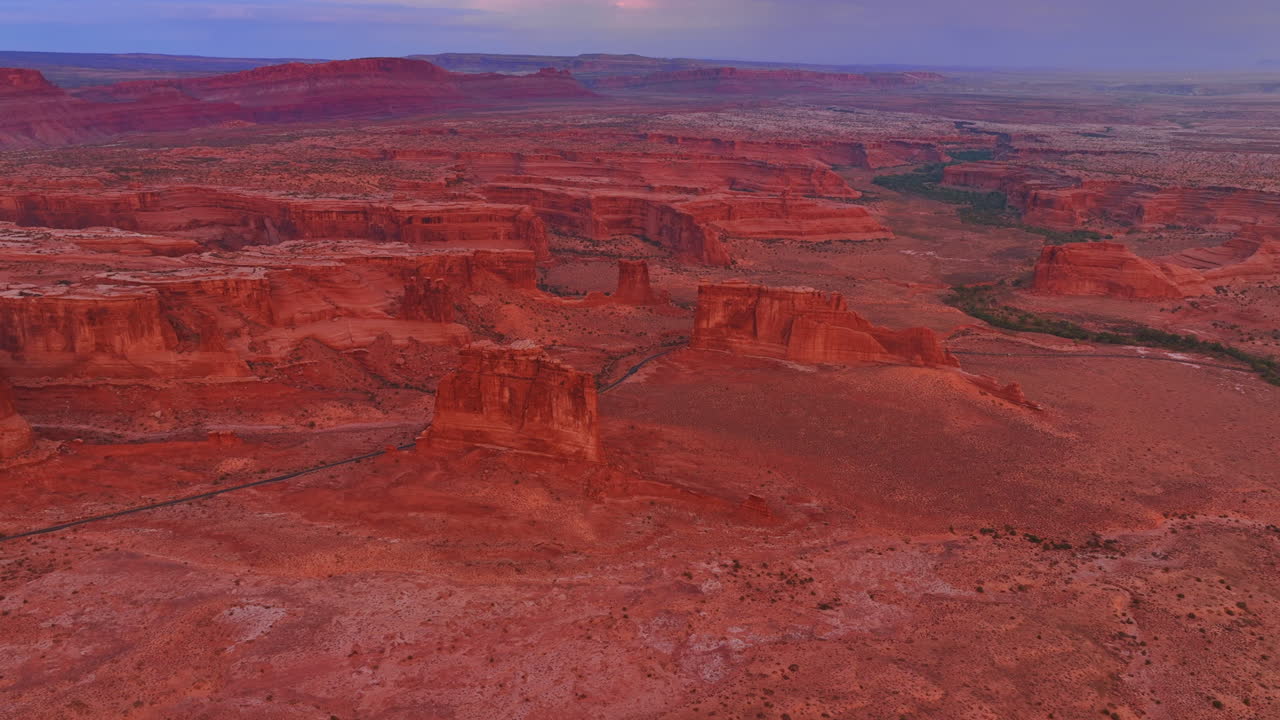 Thin line of a highway crossing the vast red deserted landscape among the stunning canyons. Drone flight above the Arches National Park, Utah, USA at sunset