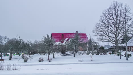casa con techo rojo entre árboles sin hojas en un paisaje nevado