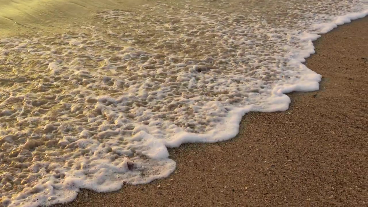 Slowmotion skummende havbølger på sandstrand ved solnedgang.