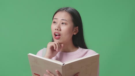 아시아 여성 학생이 책을 읽고 생각하다가 녹색 스크린 스튜디오에서 지표손가락을 들어 올립니다.