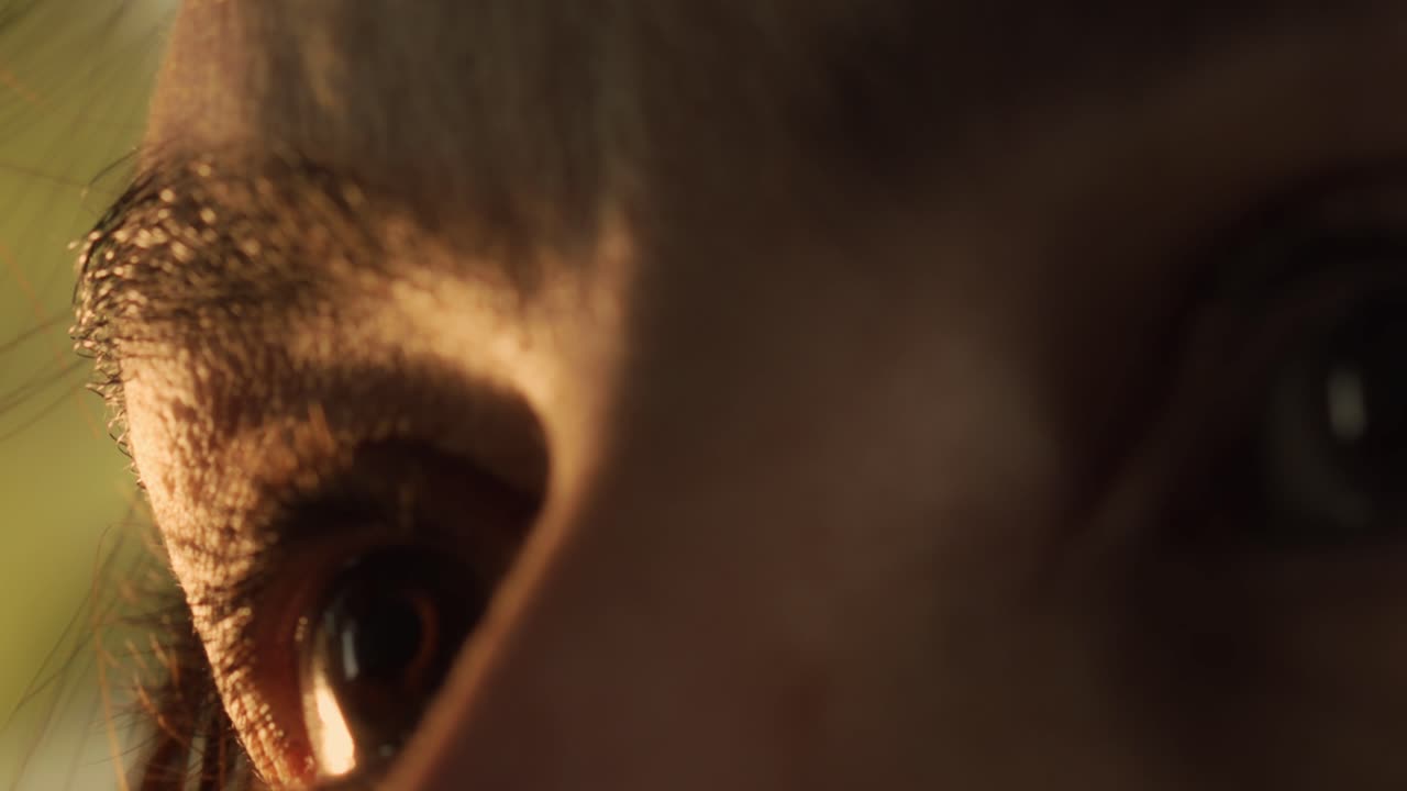 vista de ángulo bajo del ojo marrón enfocado de una mujer mientras la luz del atardecer se refleja en él