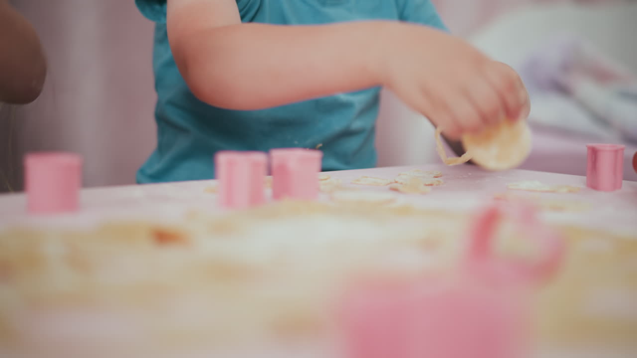 Close up of kid arranging pancake pieces on table surrounded by pink decorative dough cutters during fun creative baking activity focused on shaping and organizing playful food items