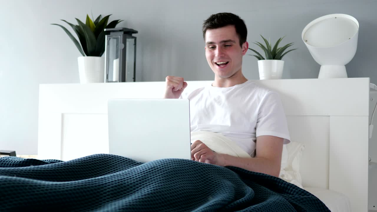 침대에 노트북을 사용하는 행복한 남자의 성공에 대한 반응