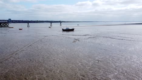 Moving-towards-small-fishing-boat-aerial-view-of-stranded-vessel-on-muddy-low-tide-on-Liverpool-coastline