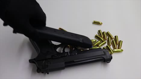 persona con un guante negro pone abajo un arma de fuego negra y que un cargador de arma de fuego en la parte superior de algunas balas