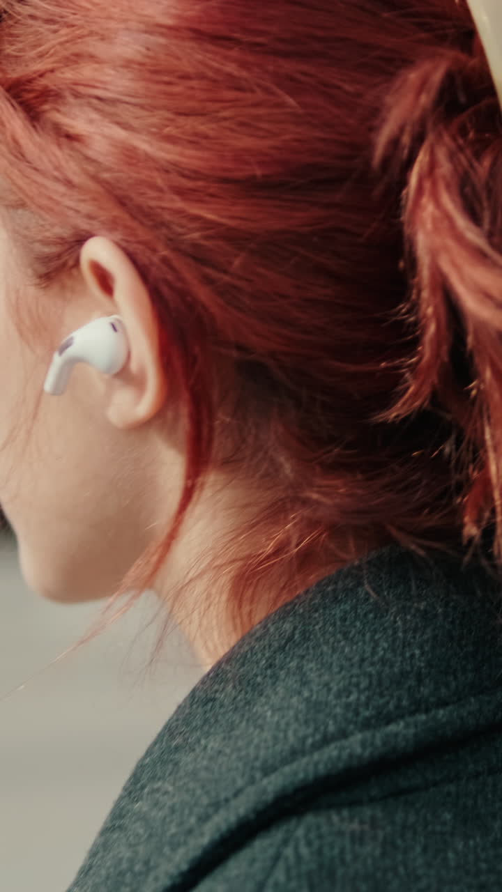 Primo piano di una giovane donna dai capelli rossi che ascolta musica con un auricolare wireless