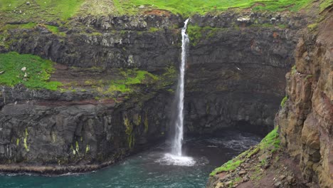 mulafossur waterfall in the faroe islands with distant view of person hiking on top of cliff