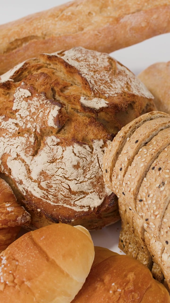Close-up slow panning shot of sourdough, baguettes, croissants, and sliced loaves on white background.