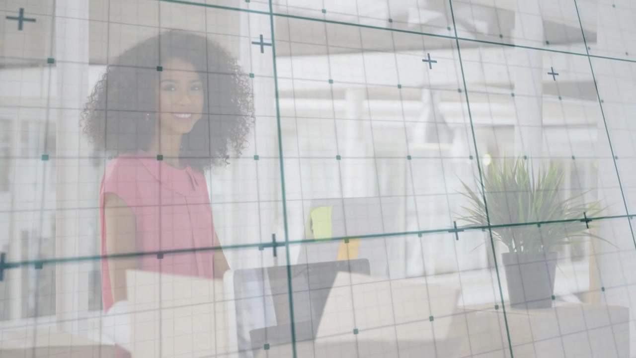 Grid overlay drifting into frame revealing woman organizing papers and using laptop in tech loft