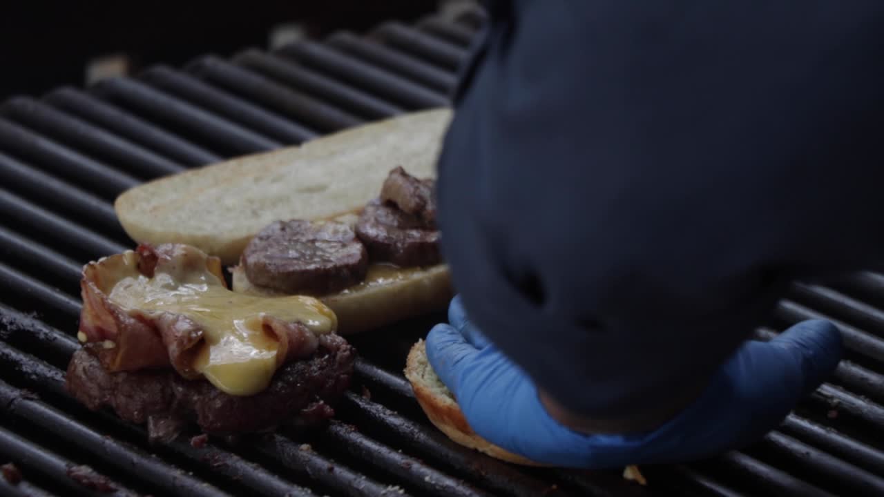 un chef cocinando un sándwich de carne, un pan de carne con queso derretido y una pieza de pan de hamburguesa en la parrilla