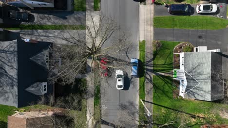 Vista-Superior-De-Drones,-Coche-Blanco-Conduciendo-Calles-De-Ciudad-Residencial-Americana-En-Patios-De-Casas-De-Primavera-En-Ciudad-Tranquila,-Ee.uu.