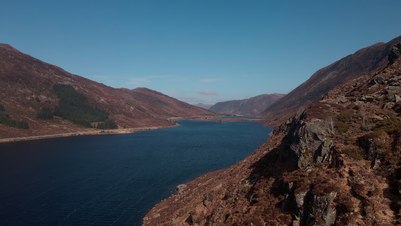 Drone flying over a lake close to a cliff on a sunny day