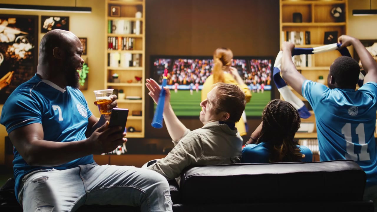Uomo sul divano con il telefono in mano che racconta agli amici il risultato negativo della partita di calcio.