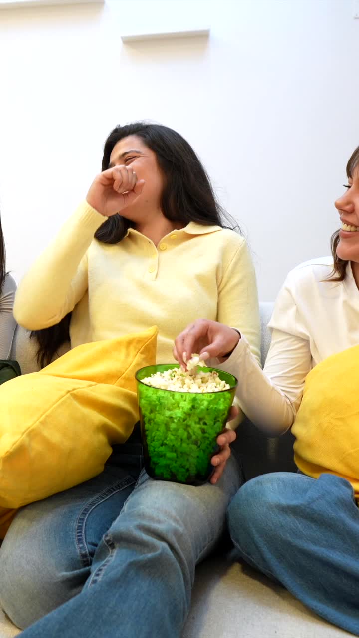 Due giovani donne ridono e mangiano popcorn su un divano