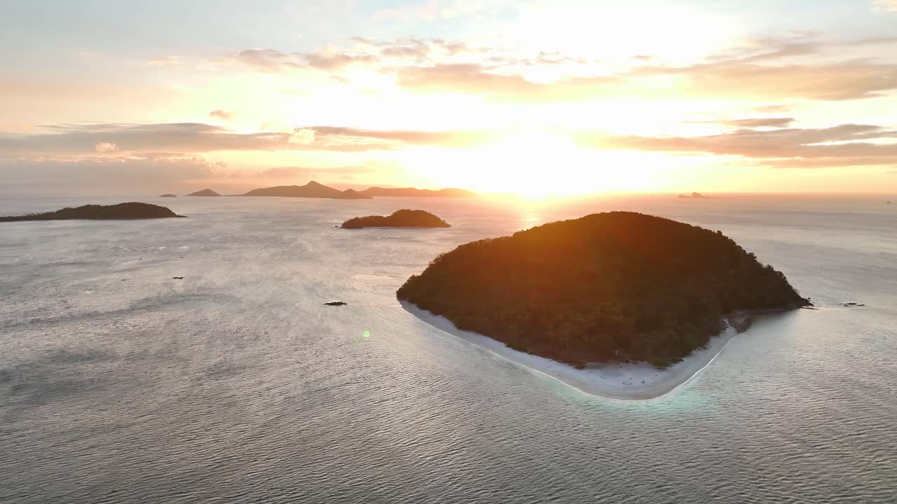 Aerial view of Cagdanao Island in the Philippines at sunset, with a lush forested hill, white sand beach, and surrounding calm sea waters framed by golden sunlight and distant islands