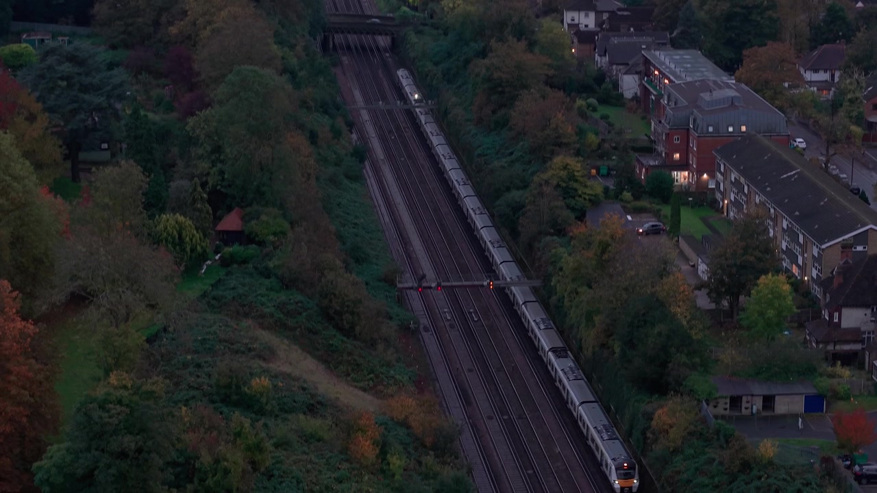 Vista aerea che segue un treno in viaggio sul binario ferroviario di Croydon attraverso un quartiere residenziale suburbano.