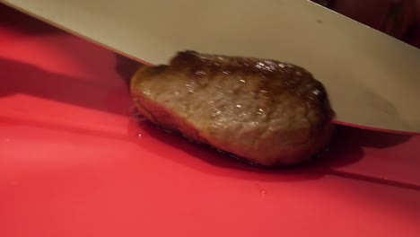 un modelo de mano masculino blanco está cortando una carne de cordero cocida en una tabla de cortar roja