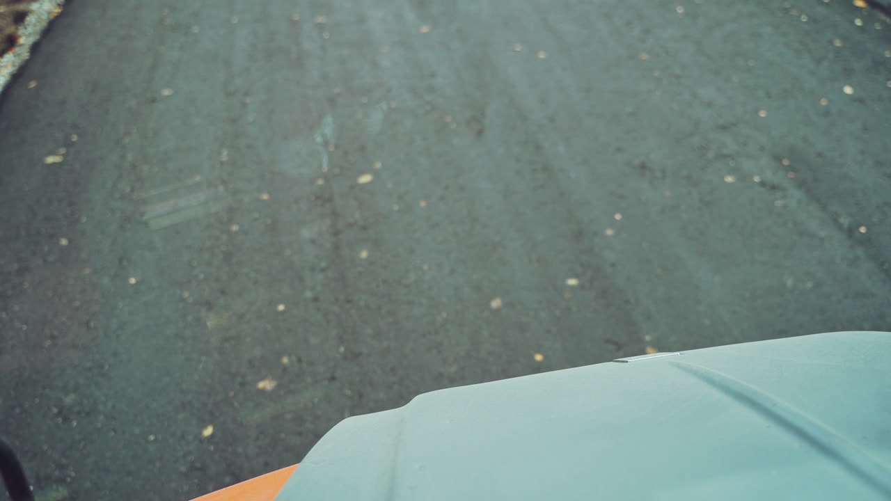 Close-up view through the window truck of a new asphalt on the natural background of autumn trees. New bitumen is laying on the road by special machinery equipment and technics.