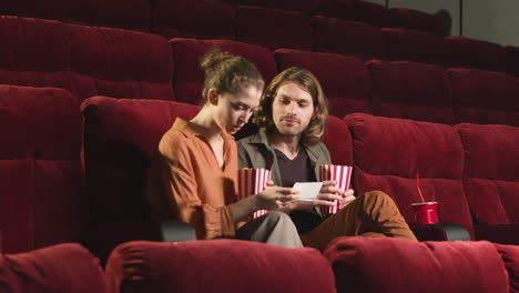 couple sitting on the seats in the cinema while they holding popcorn and drinks and waiting to watch the movie